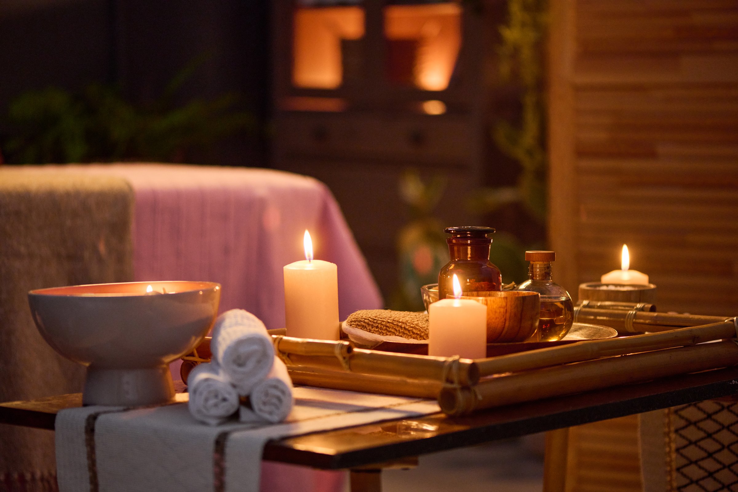 Medium close up of small coffee table with towels rolls, wooden tray with aroma candles and oils in massage room