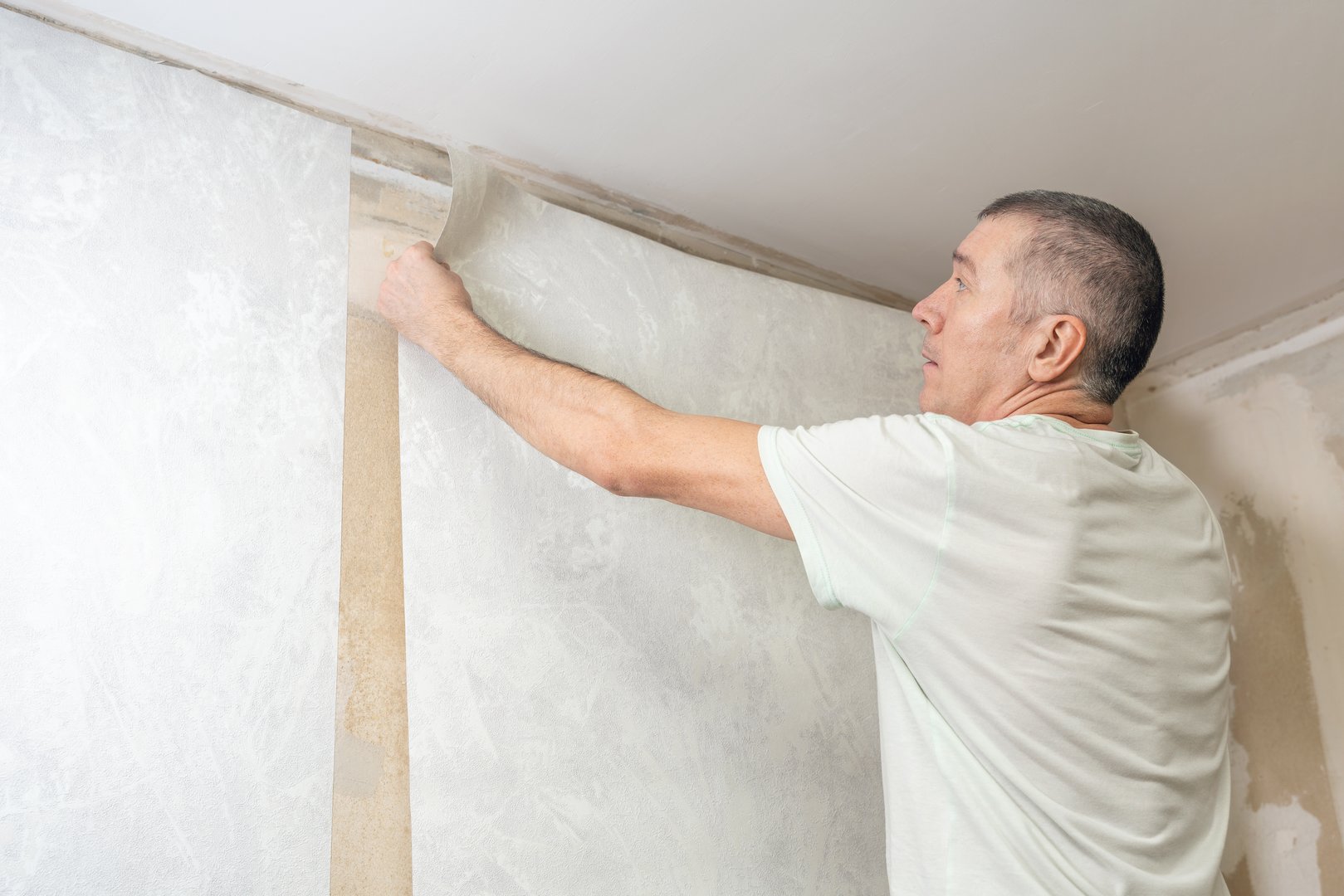 A man is gluing non-woven wallpaper on the wall. Room renovation.