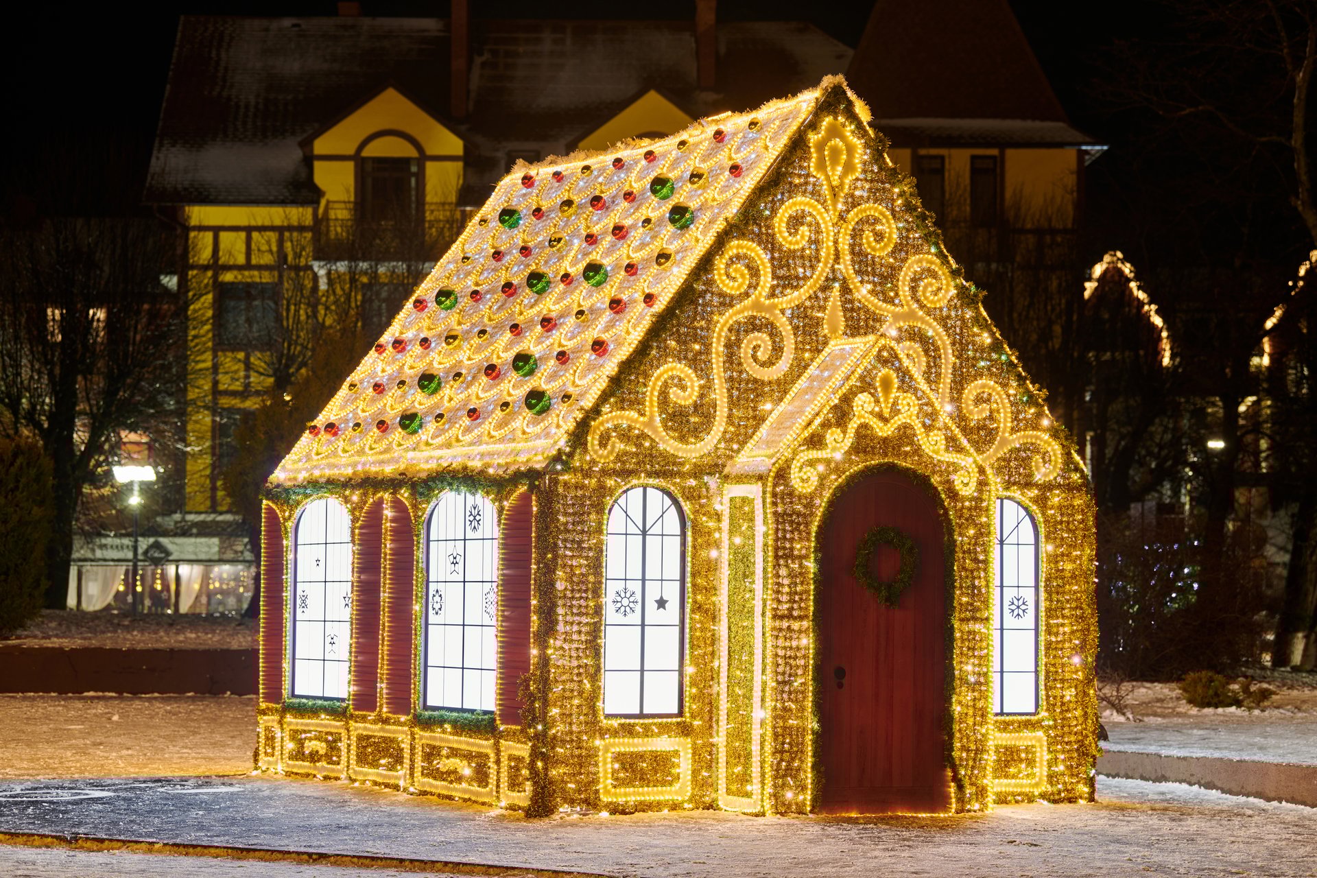 Small fairy tale house decorated with twinkling garlands lights and glittering patterns, night city street Christmas decoration for happy New Year mood, yellow flickering lights at house exterior