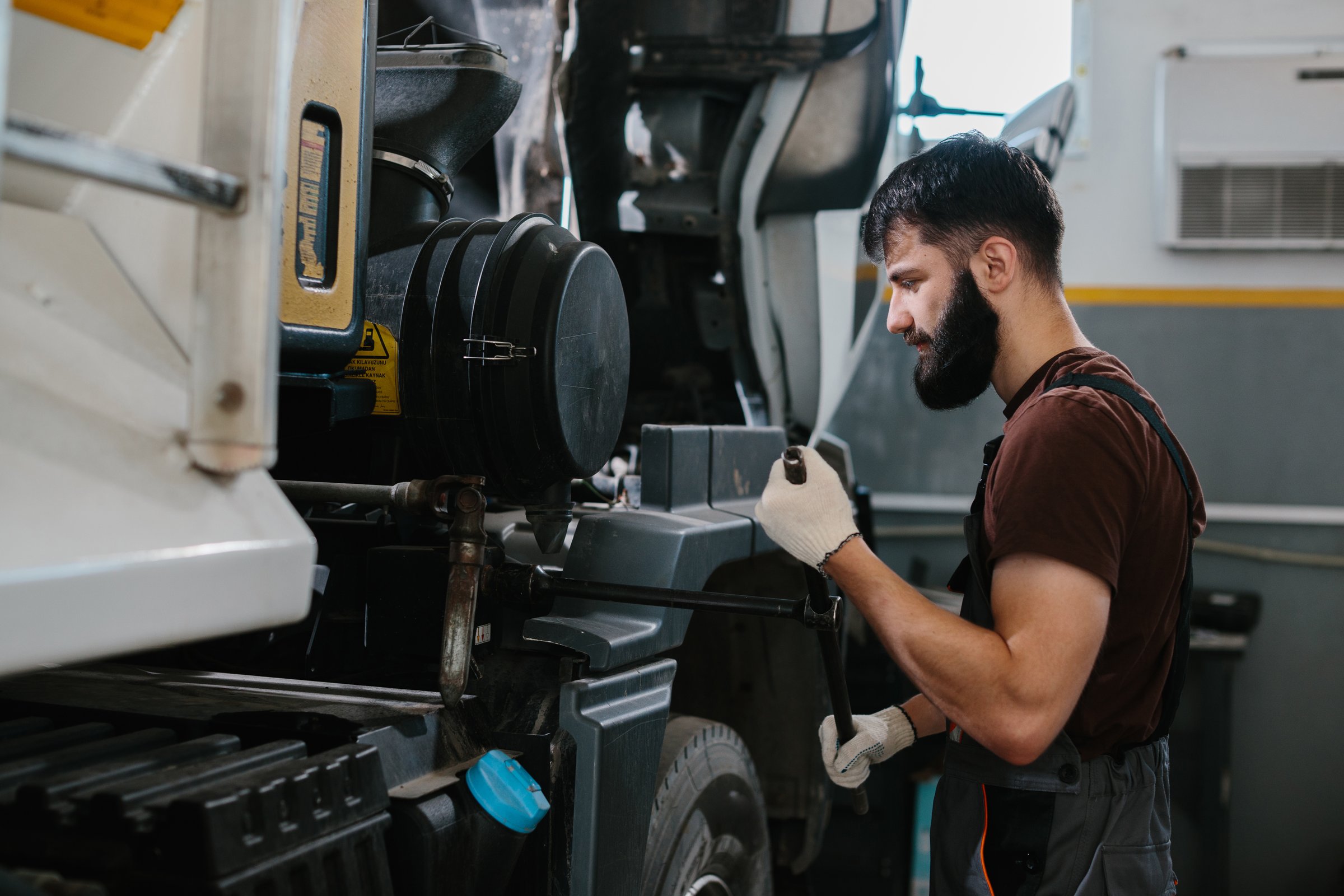 Professional mechanic working on a truck engine inside a garage workshop, using tools and expertise to ensure proper maintenance and repair