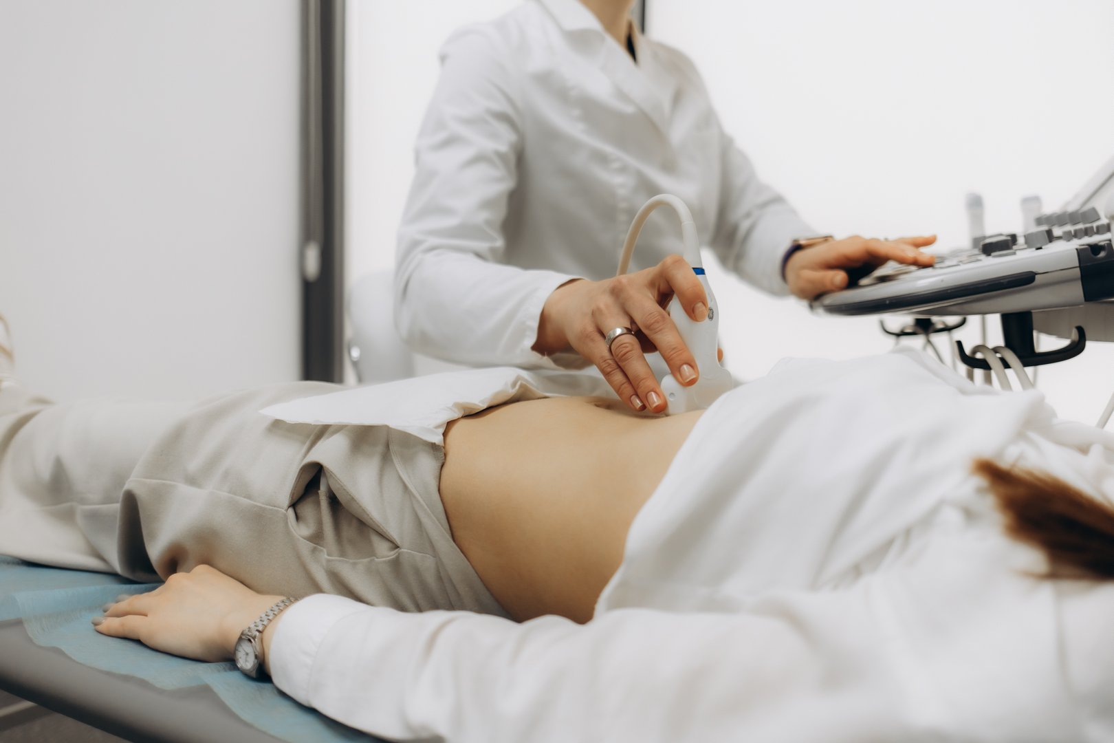 Closeup of male doctor moving ultrasound probe on pregnant woman's stomach in hospital