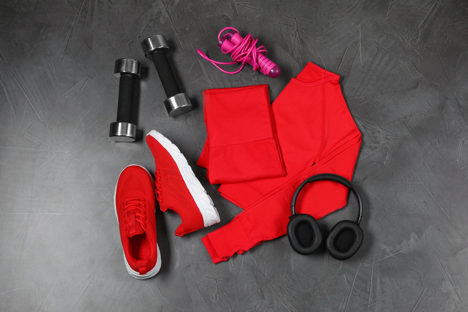 Stylish sportswear, dumbbells, red sneakers, skipping rope and headphones on grey background, flat lay