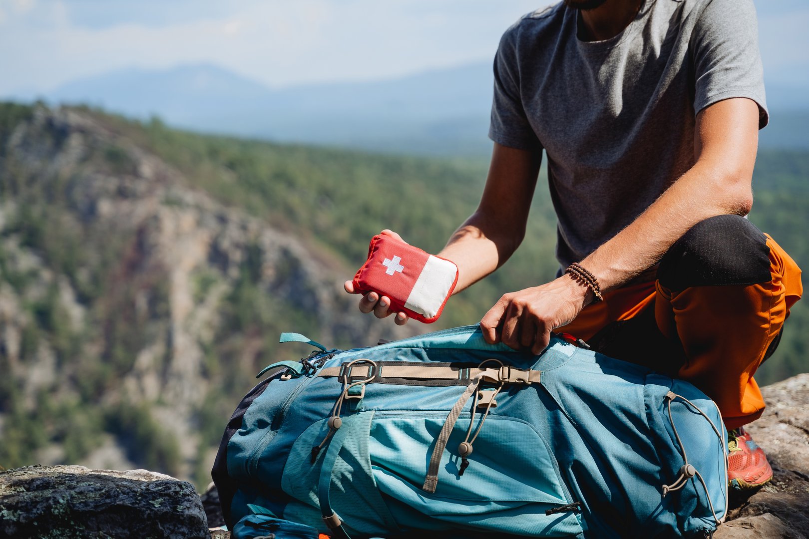 Take a first-aid kit in a backpack on a trip, a hand holds a first aid kit against the background of mountains, equipment in an extreme hike, a white cross. High quality photo