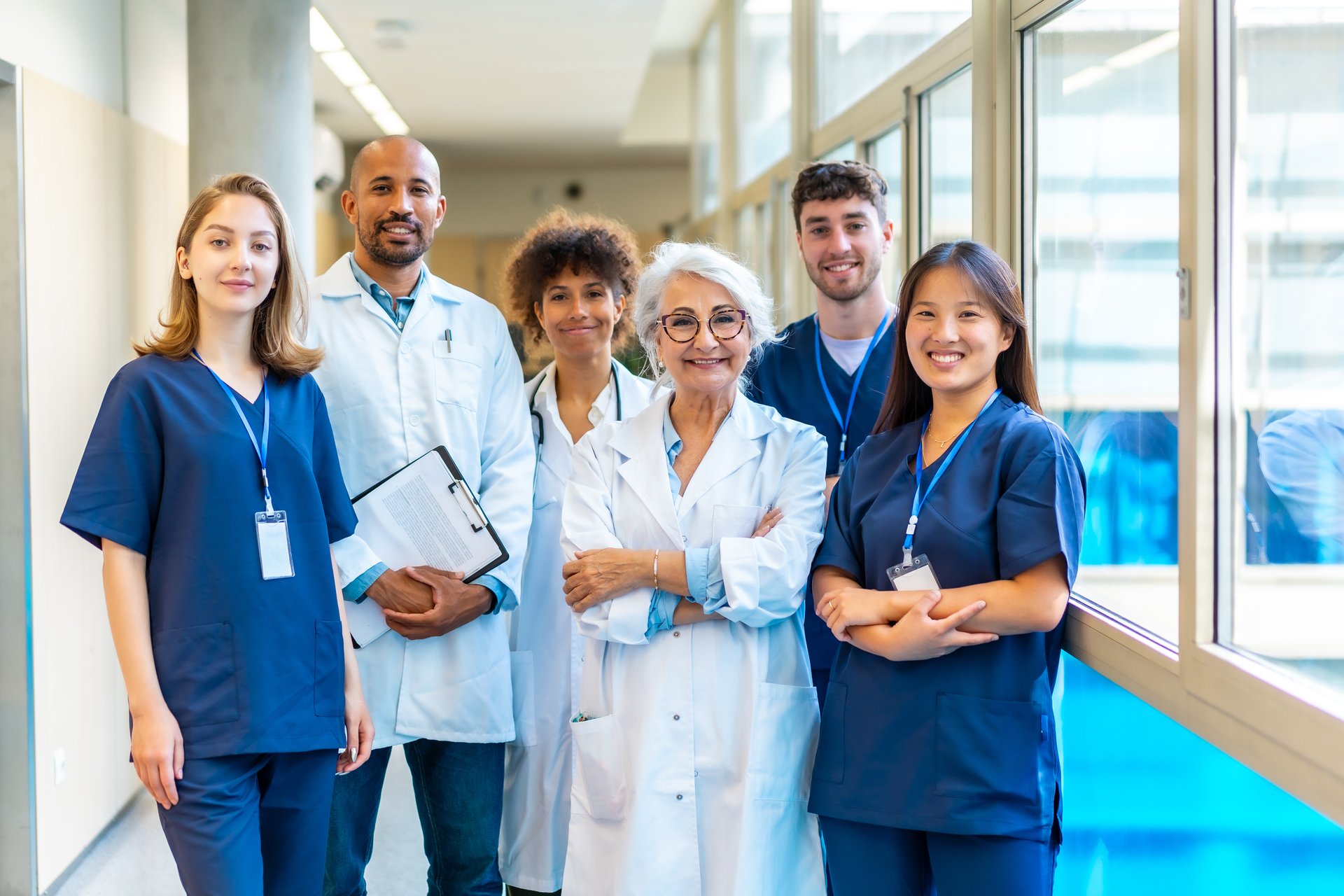 Portrait featuring a multi-ethnic medical team smiling confidently at the camera while gathered in a bustling hospital corridor