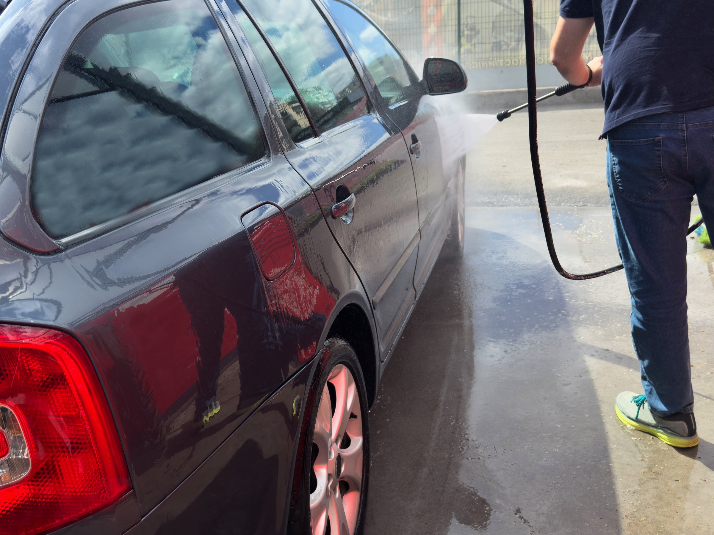 Close-up of car wash process. Man directing hose with water stream to his car, washing car at car wash. Car wash concept. People and transport