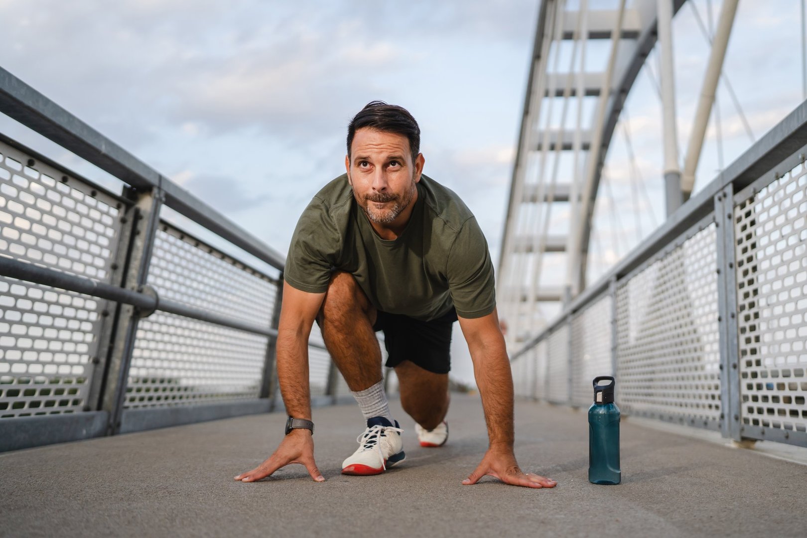 Mature man in starting position on an urban bridge, focused and determined, preparing for a run that showcases fitness, endurance and a healthy, active lifestyle in the city