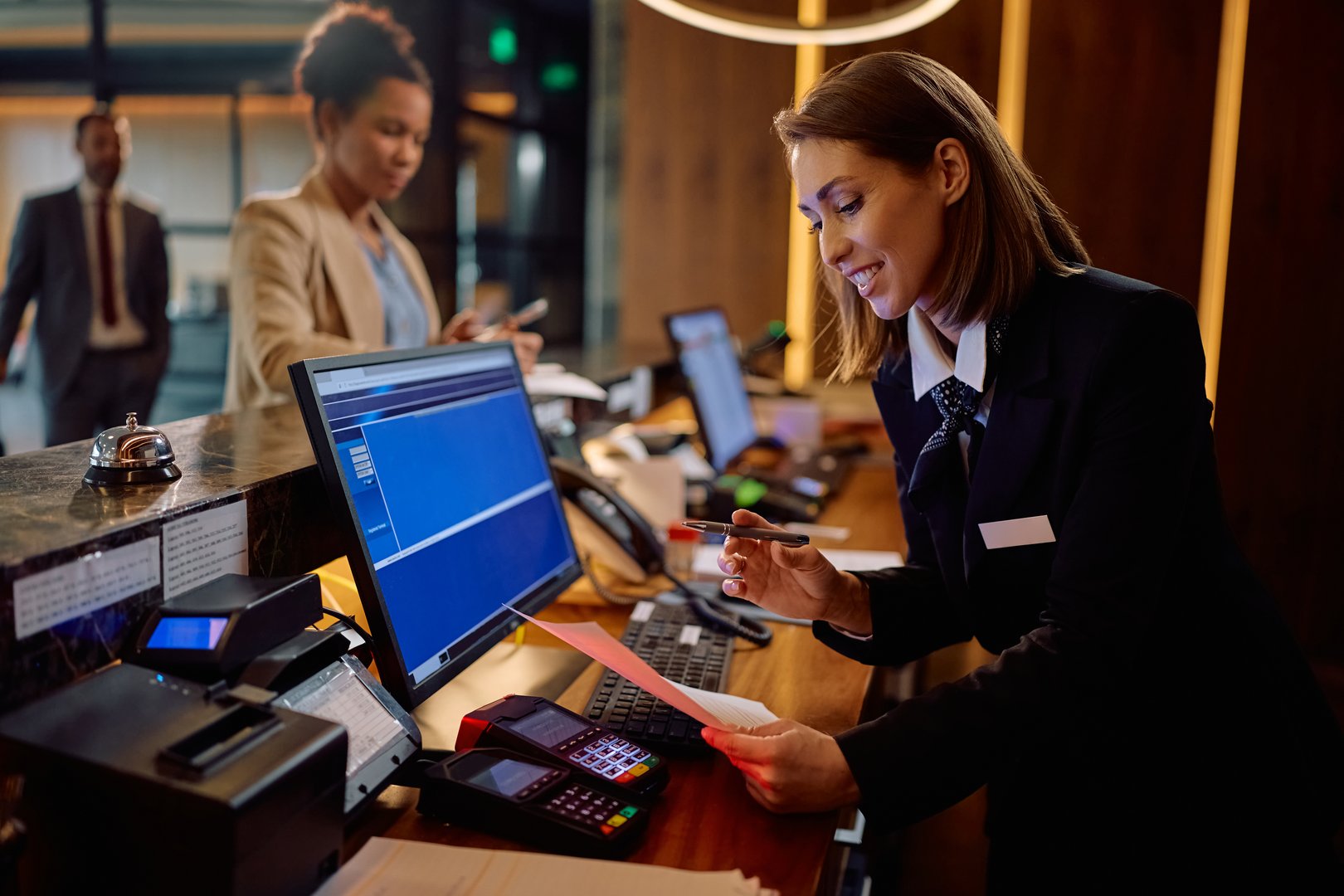 Happy hotel manager filling out registration documents during guest check in at reception desk.