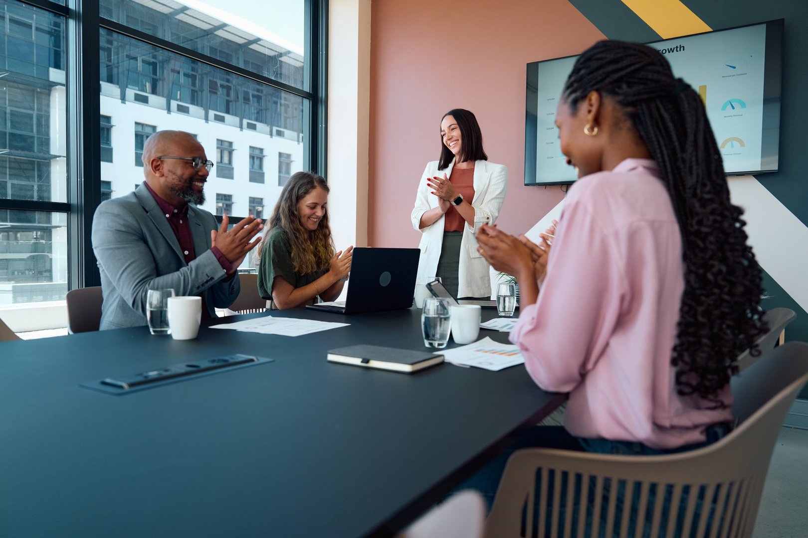 Diverse team of Black African professionals in smart casual attire applauding while businesswoman presents in modern boardroom