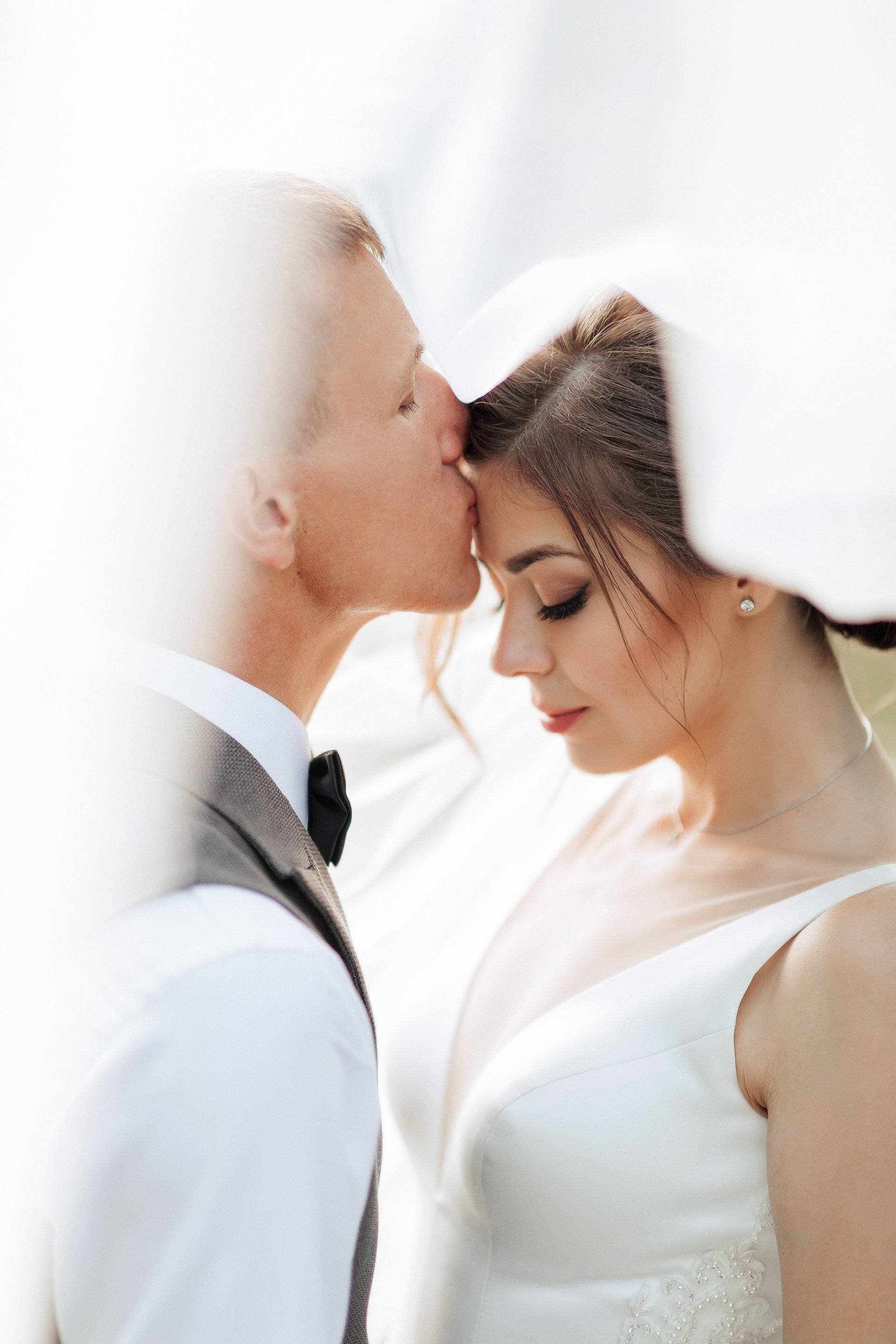 A bride and groom kiss each other. The bride is wearing a white dress and the groom is wearing a suit