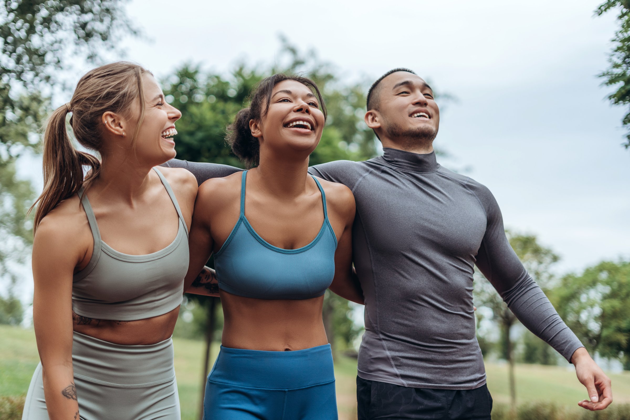 Diverse group of happy, attractive sportspeople wearing sportwear hugging together. Smiling friends after training outdoors. Sport, motivation concept