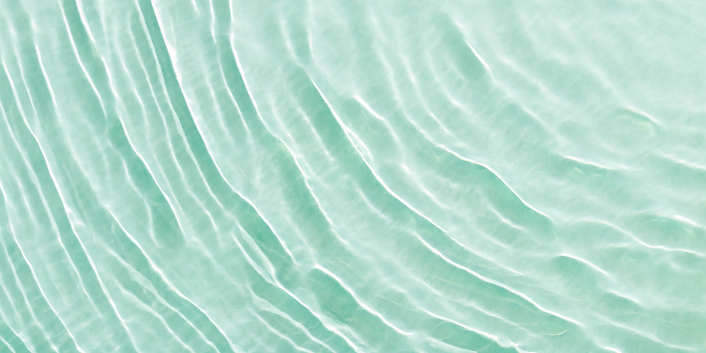 Close up view of sunlit water surface with gentle ripples with light reflections. Crystal clear water with sunlight soft wavy patterns. Abstract nature minimal background, natural textured banner