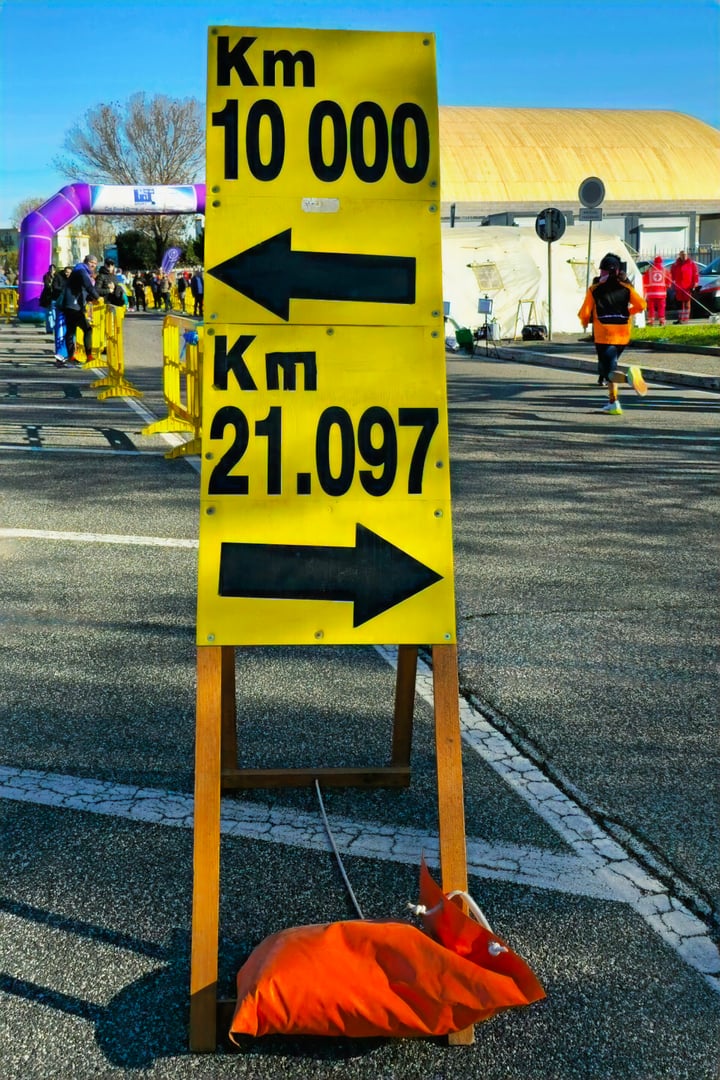 Fiumicino  - December 1, 2024: Directional signage for runners during a sports event, marking 10K and 21.097K routes. In the background, the finish line of the Fiumicino Half Marathon organized by Cat Sport Roma