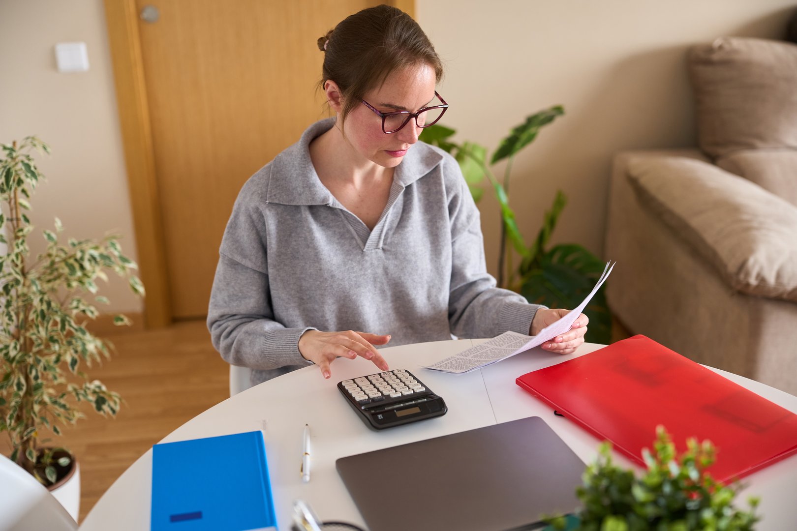 Young woman working with calculator and documents at home office, managing finances and accounting tasks