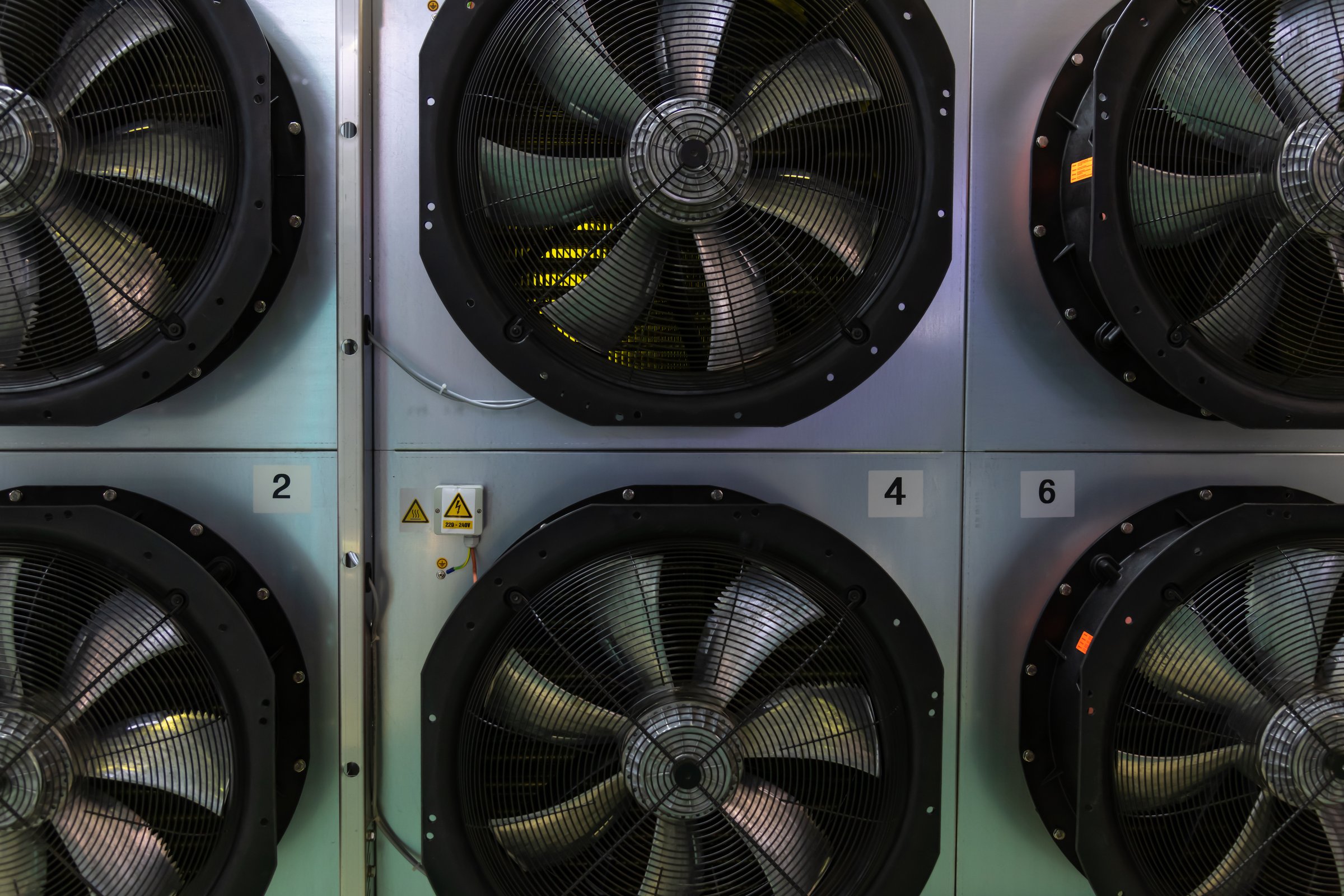 Several large cooling fans are positioned on a wall in an industrial setting. The fans are used for air circulation and temperature control, highlighting advanced technology and efficiency.