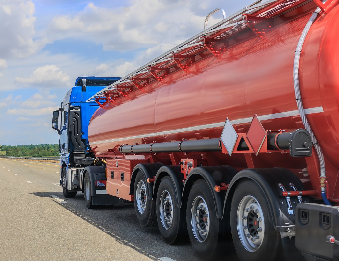 fuel truck moves along a country highway on a sunny day under a blue cloudy sky