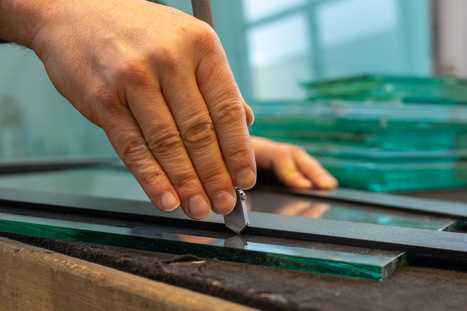 Work in a glass factory. A glazier cuts glass. Close up. A hand holding a cutter.