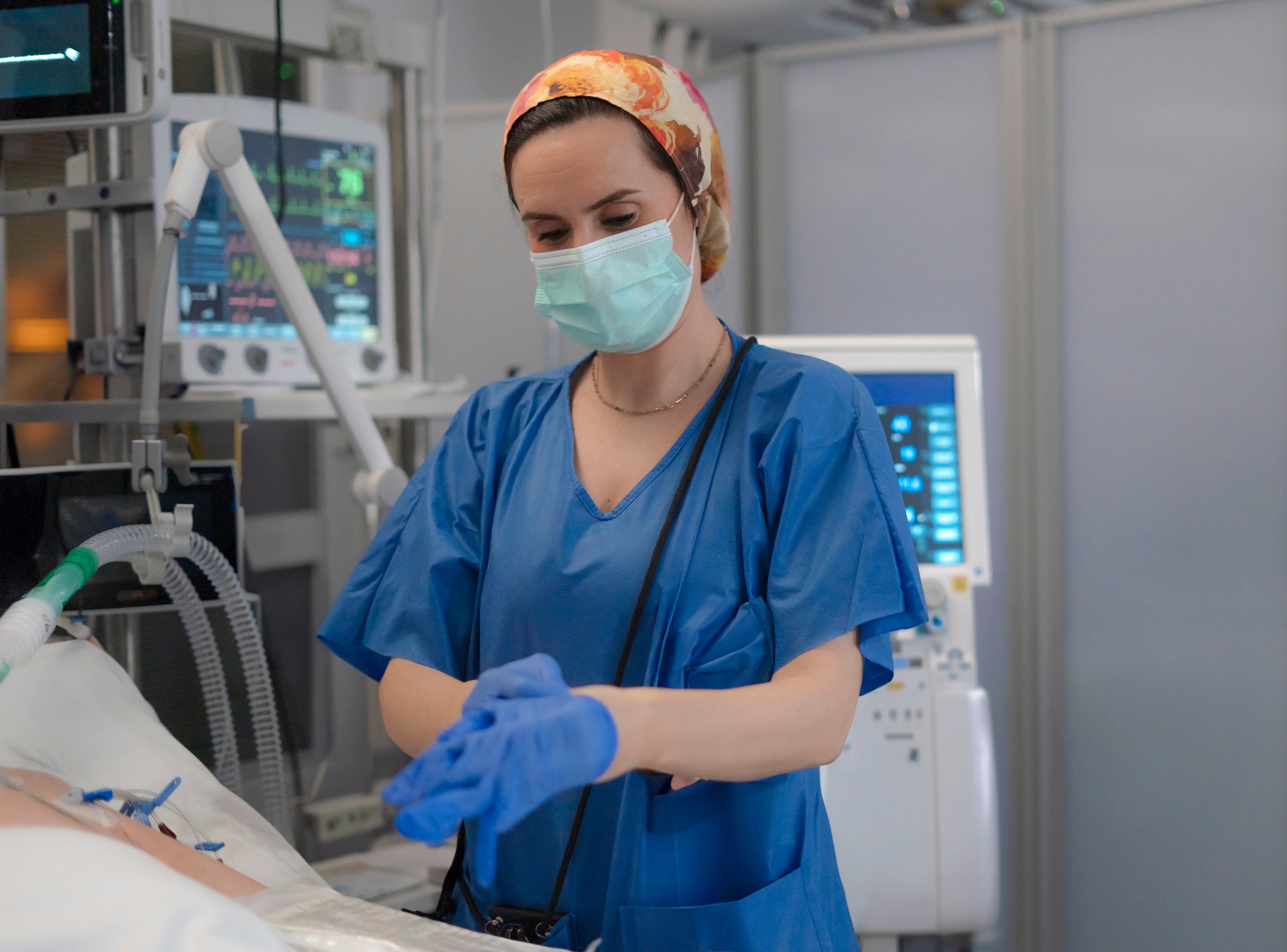 Female nurse putting on blue sterile gloves in hospital operating room, getting ready for surgery