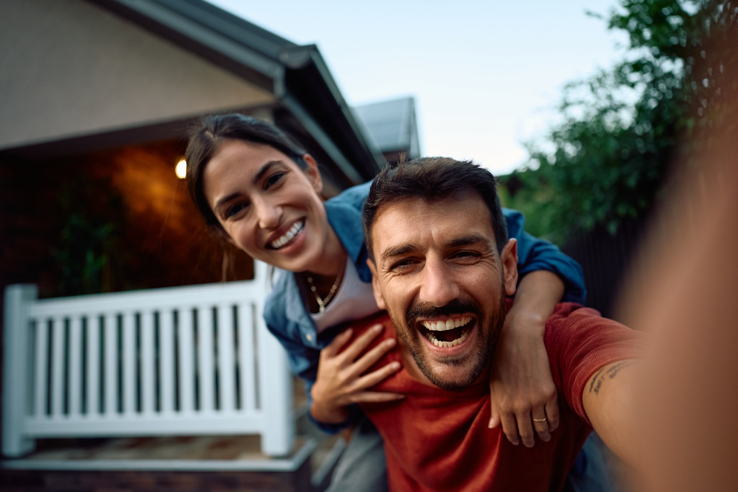 Happy new homeowners having fun while taking selfie in the backyard and looking at camera.