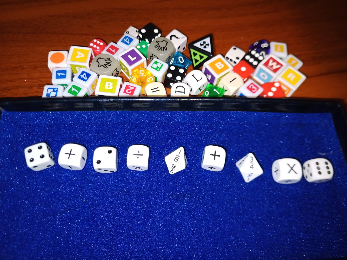 Various colorful custom dice and symbols on a wooden table next to a blue dice tray with white dice.