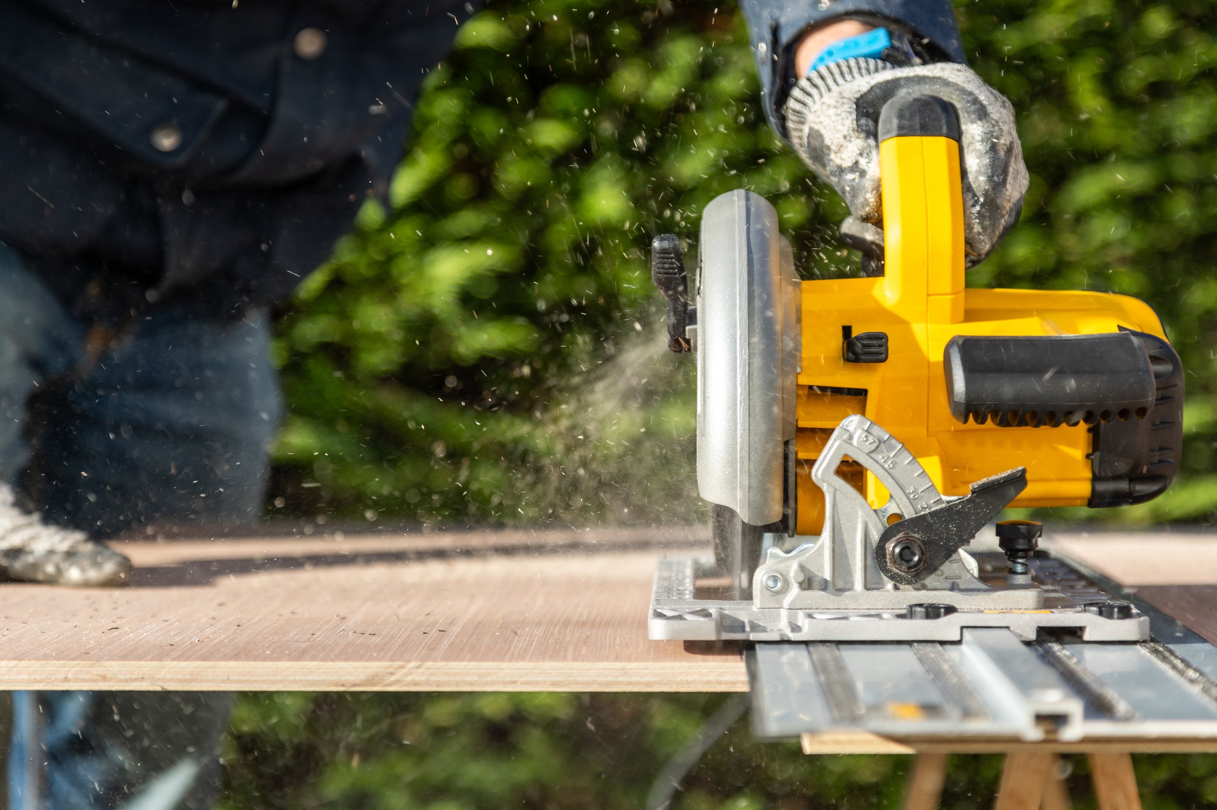 Male doing DIY carpentry using an electric circular saw with aluminium guider on wood sheet material outside in sunshine