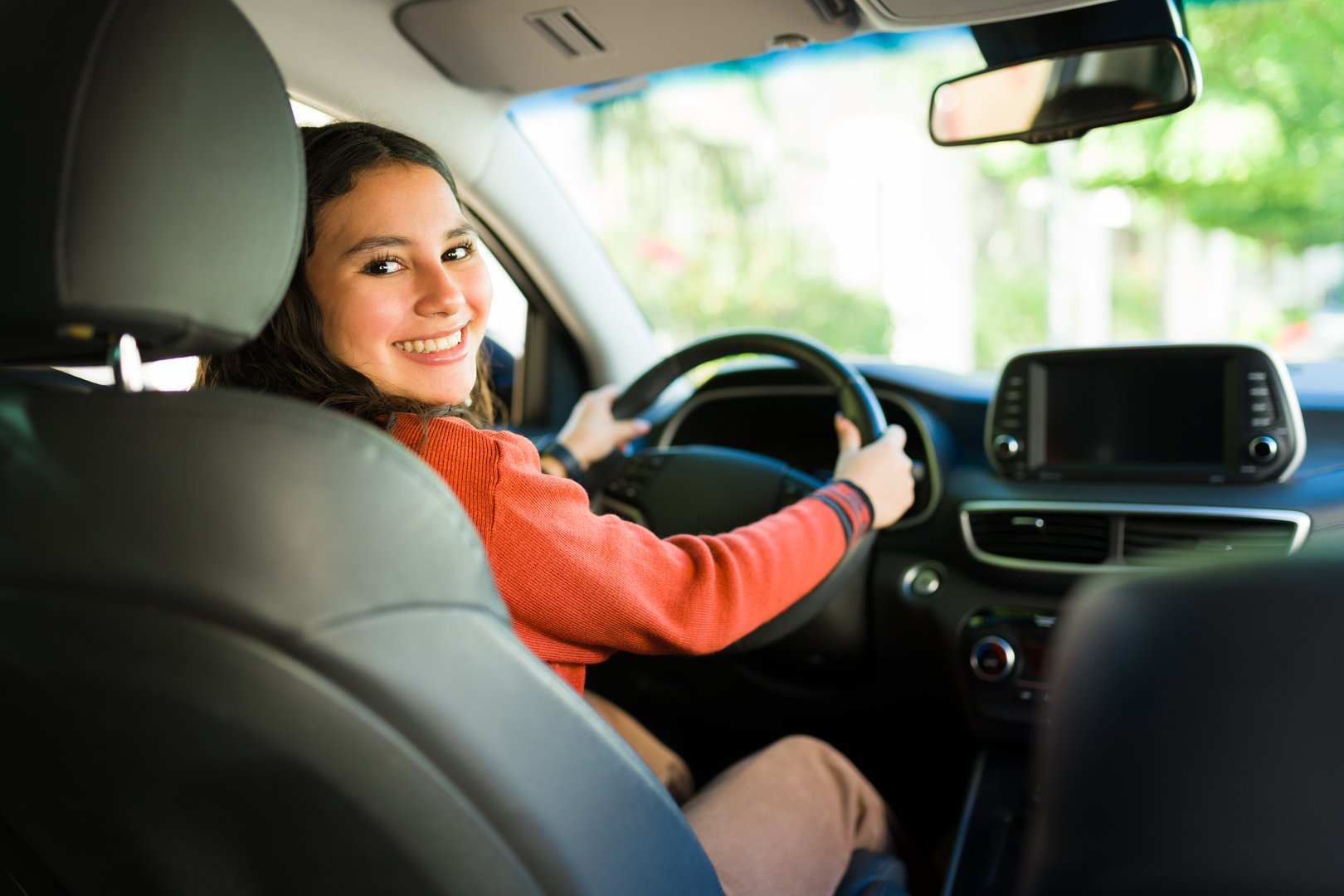 Portrait of a cheerful teen girl enjoying driving a car and smiling at camera while sitting in the driver's seat