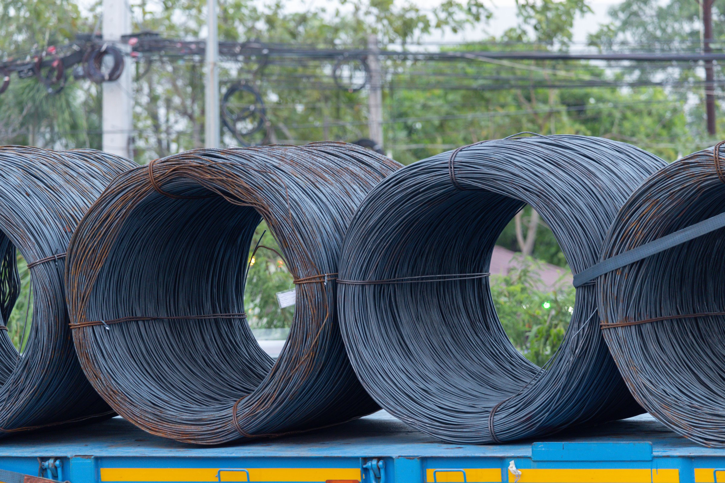 A row of metal wire is stacked on a blue truck. The wire is black and rusty. Scene is industrial and somewhat bleak