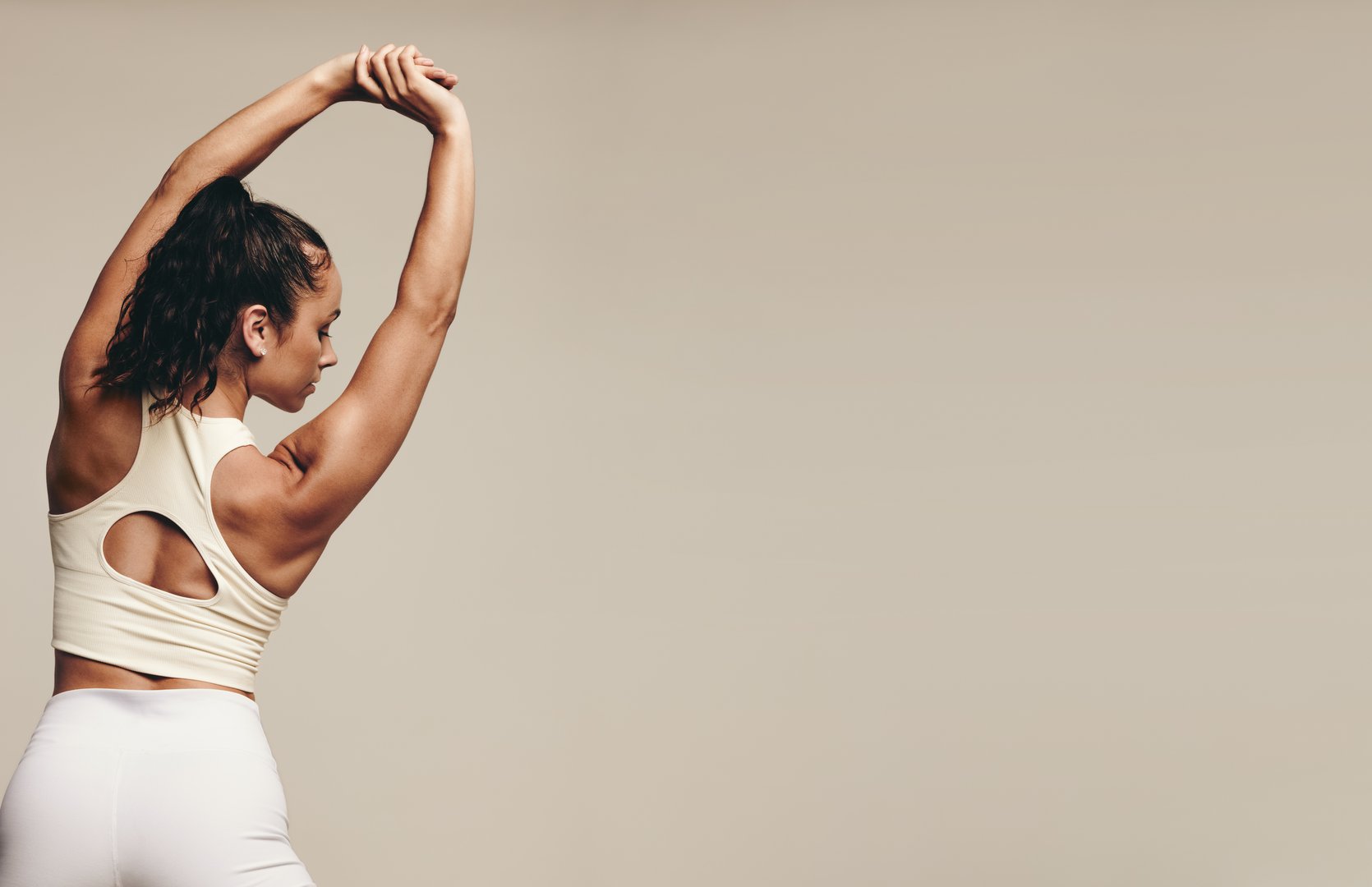 Sporty young female working out with muscle-toning stretch exercises in a studio. Athletic young woman striving for better flexibility and balance through regular strength training.