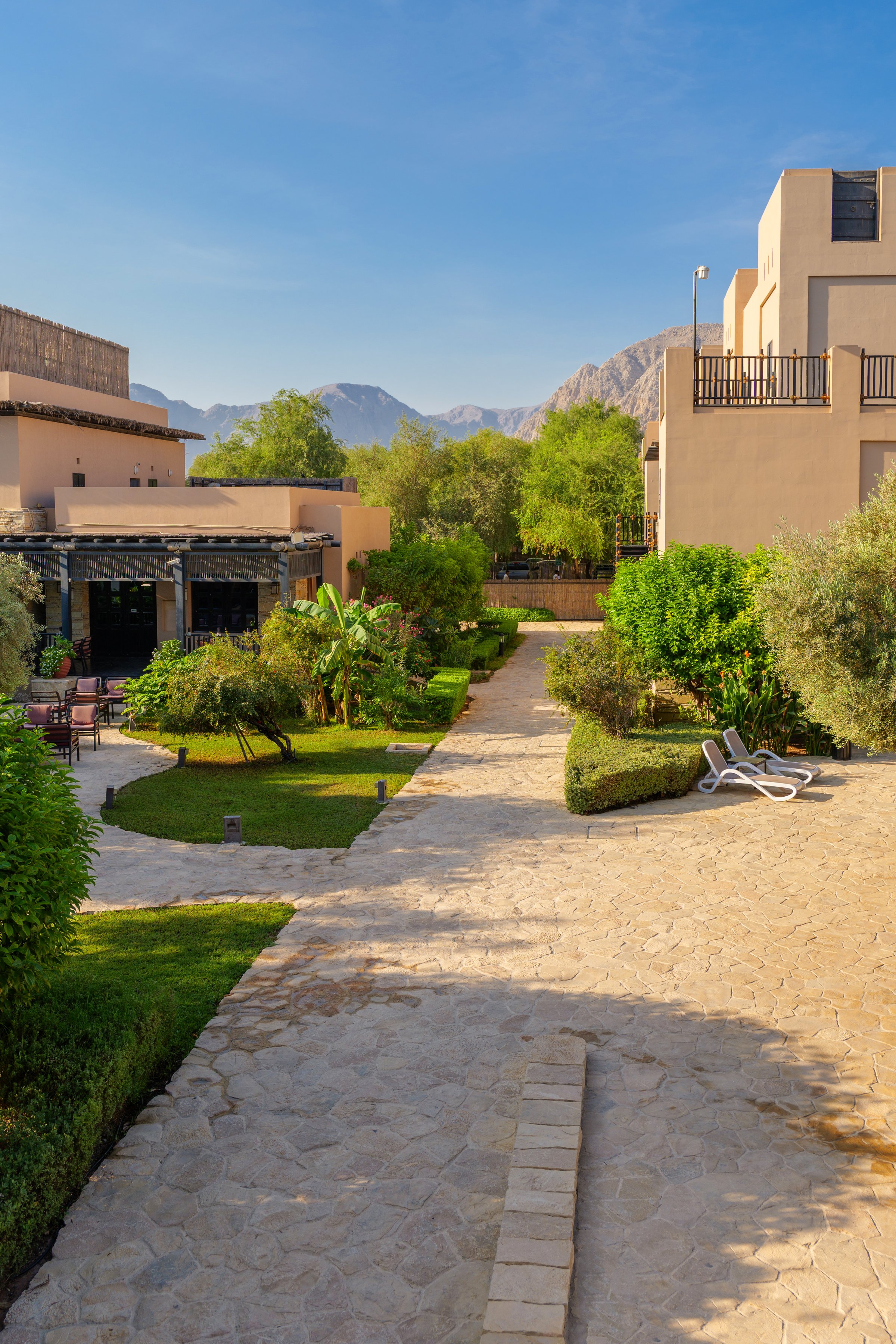 outdoor view of a resort area with stone pathways, lush greenery, and modern beige buildings. High quality photo