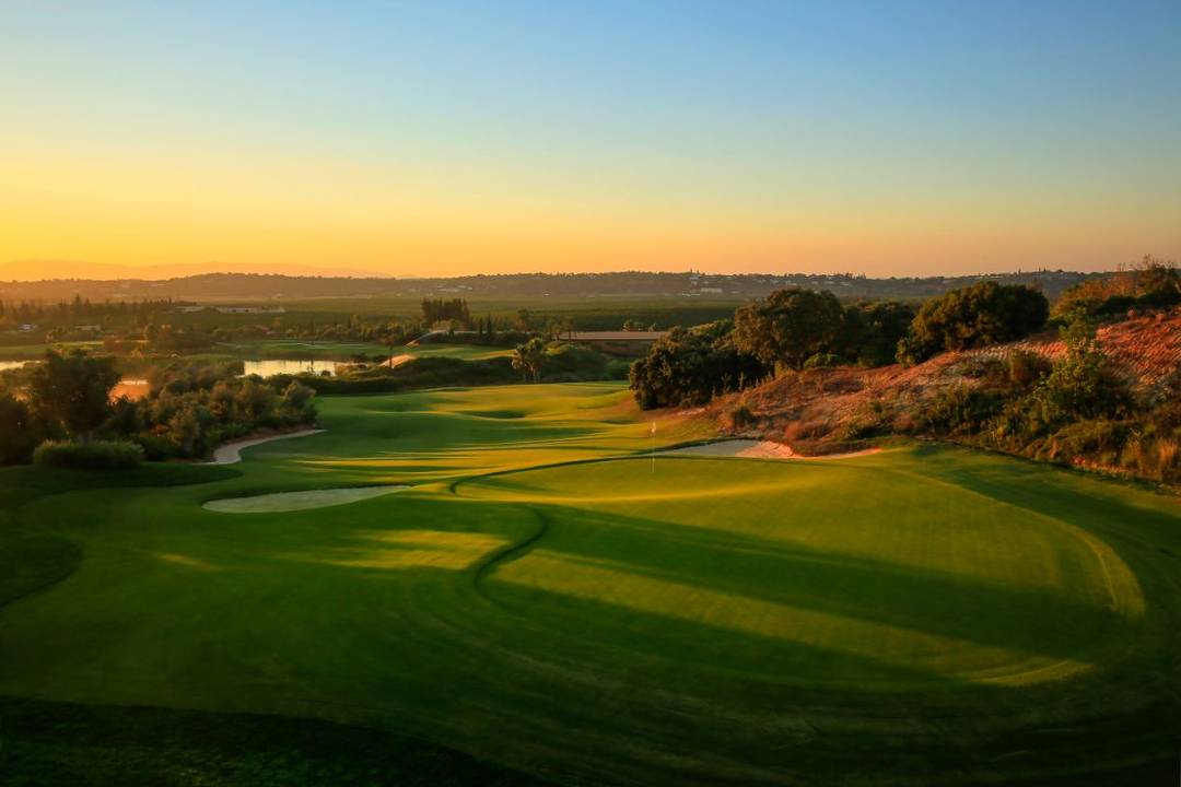 Aerial view of luxury beachside resort with golf course in Portugal, featuring lush green fairways, pristine beaches, and elegant resort buildings along the coastline