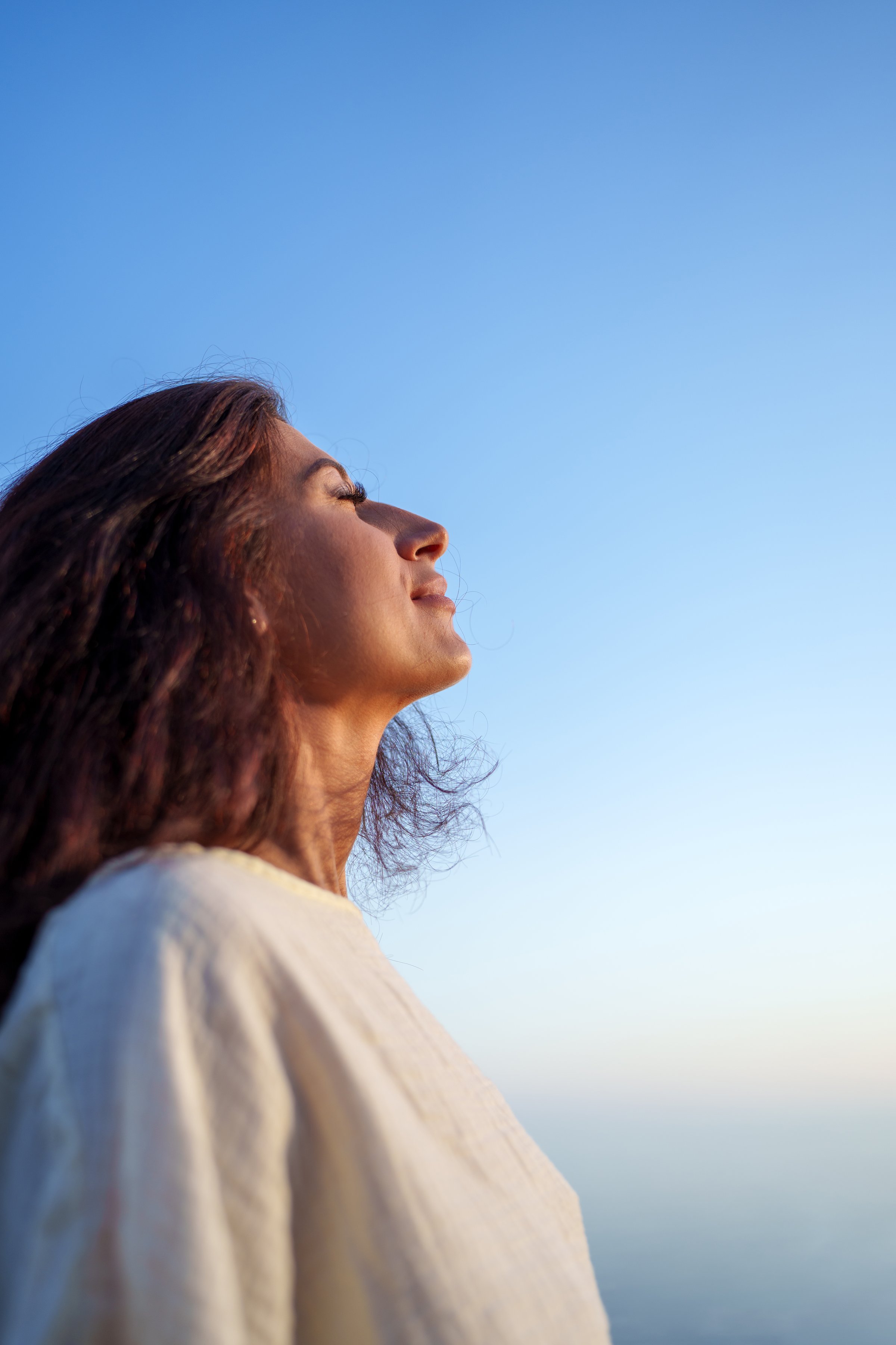 Side view portrait of a young woman breathing deeply fresh air with closed eyes against a blue sky