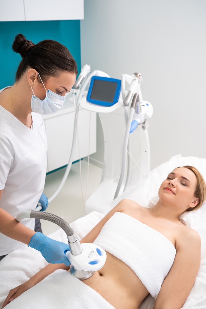 High angle of Caucasian masseur wearing blue rubber gloves and making massage procedure on belly of her client. Cropped photo of female patient lying on massage table. Body weight loss and anti cellulite concept