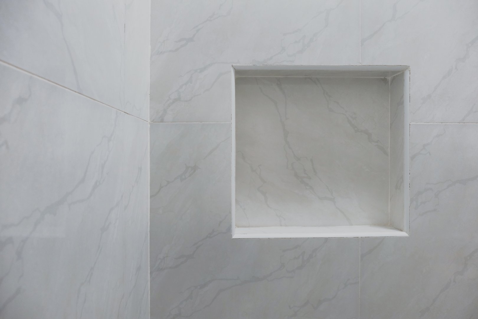 Close up of empty built-in shower caddy in wall recess in bathroom. Modern elegant bathroom interior with marble wall tiles. Display shelf for toiletries logo branding mockup.