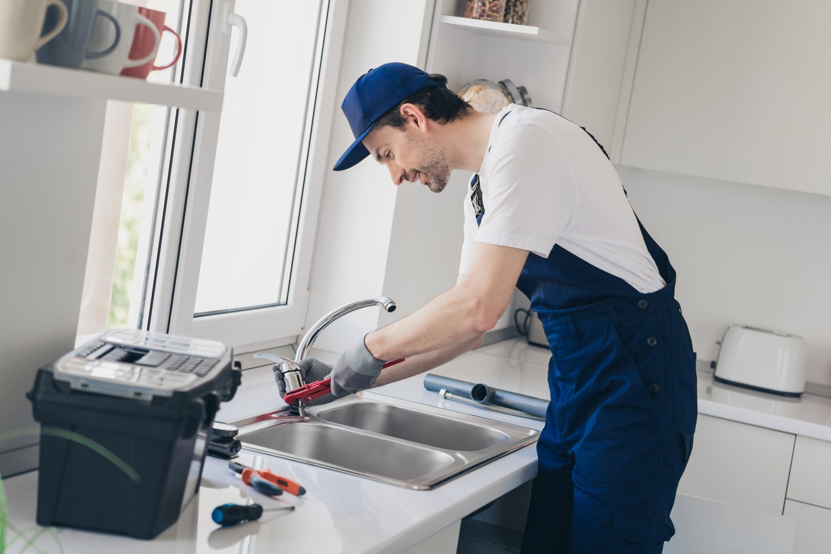 A professional handyman expertly repairs a kitchen sink in a contemporary home, showcasing technical skill and attention to detail in plumbing. Ideal for renovation and maintenance concepts.