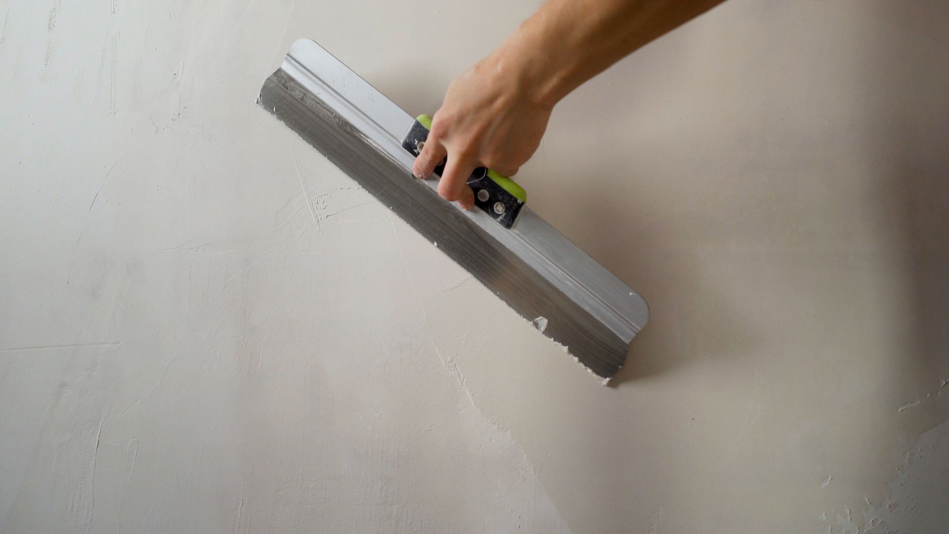 Construction worker smoothing wet plaster on wall using a spatula, during renovation or construction work
