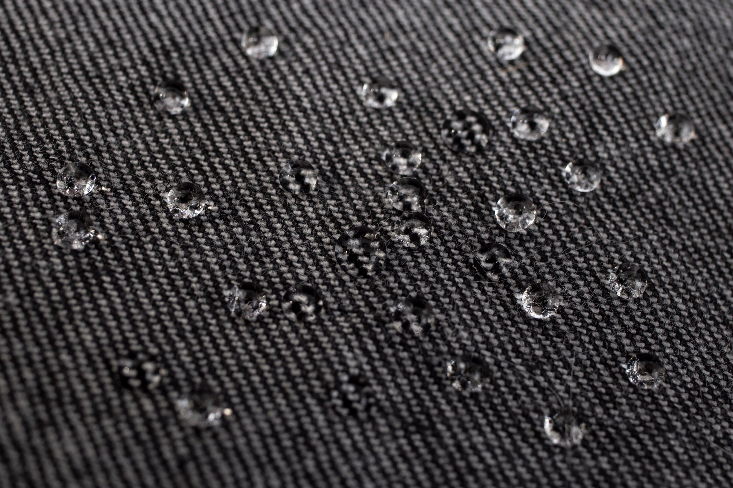 Black jeans fabric texture with water drops on the surface, impermeability concept, soft focus