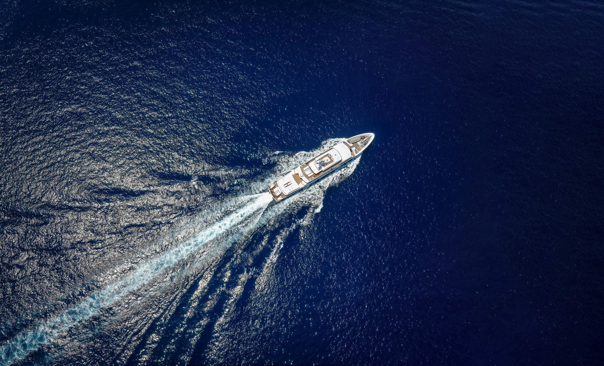 Aerial top view of a luxury yacht cruising with high speed over blue ocean