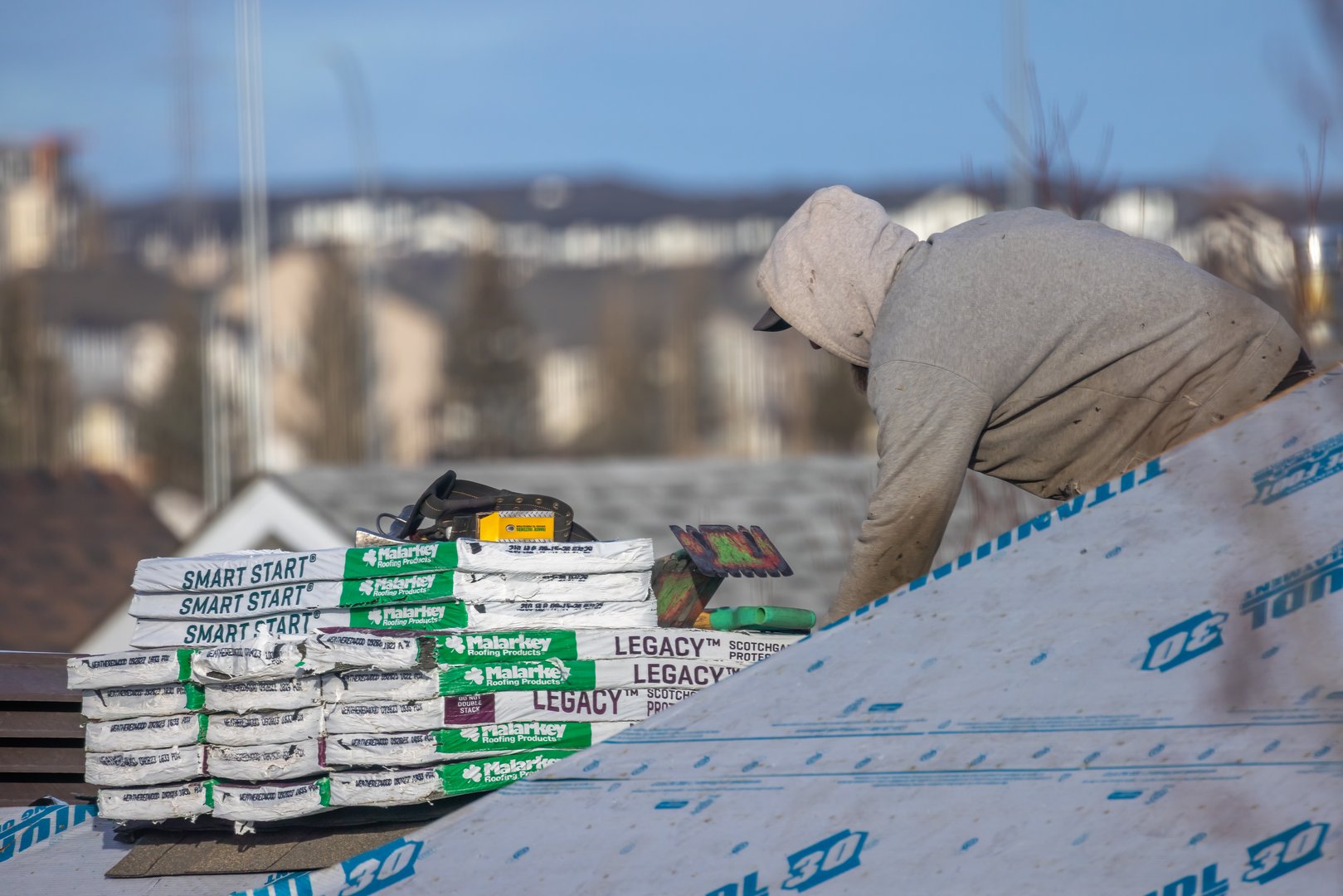 Calgary, Alberta, Canada. Apr 6, 2025. A roofer installing roofing materials on a pitched roof. Stacks of Malarkey shingles and other supplies are visible.
