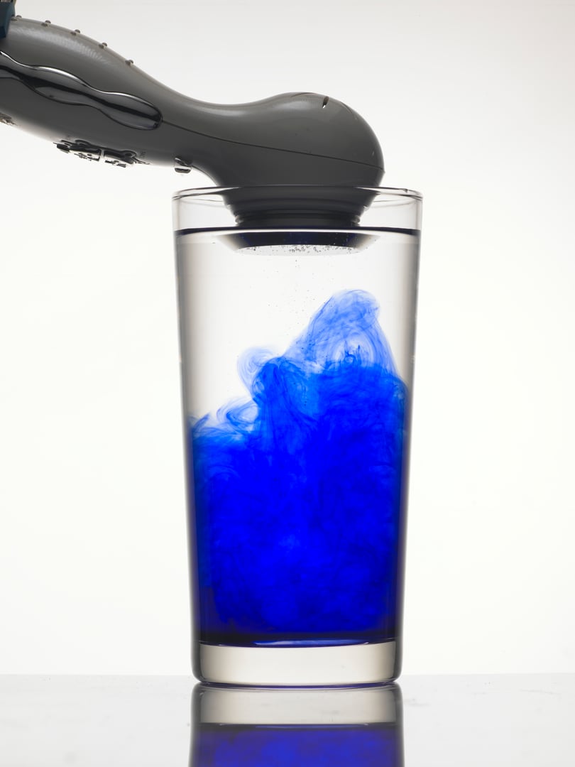 Vibration creates abstract form of blue color in glass of water.