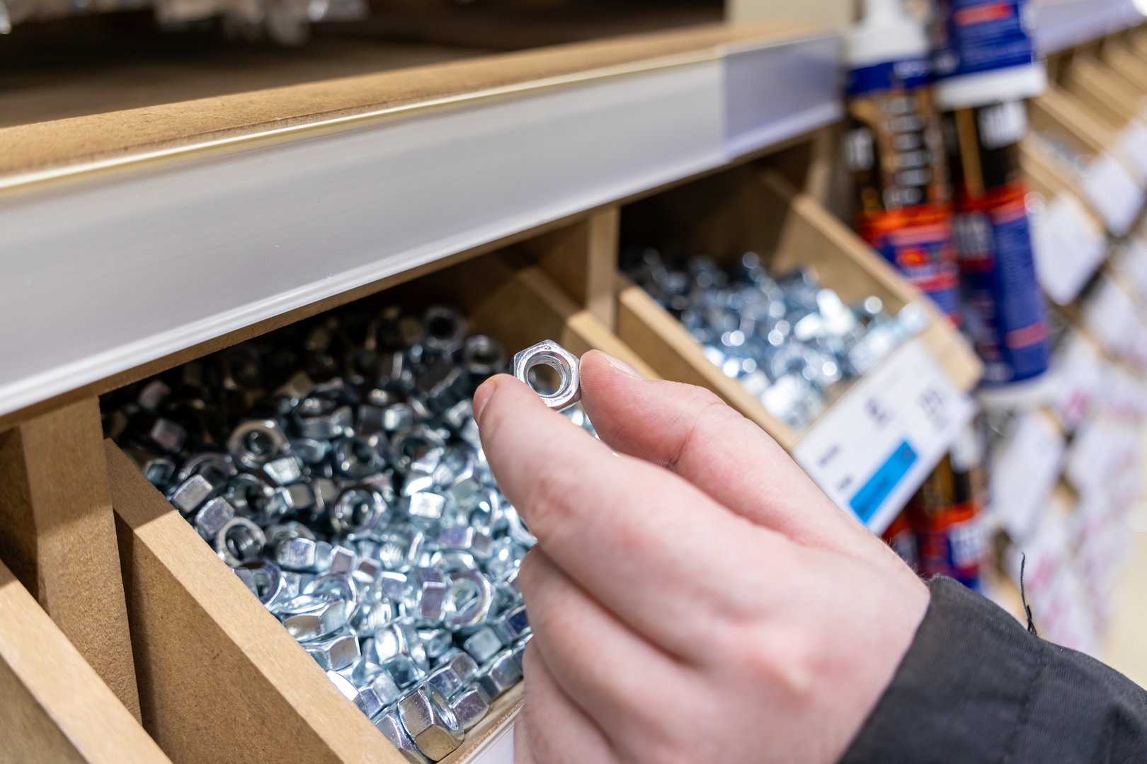selection of a metal nut from a wooden box in a hardware store, close-up of fastening materials for construction and repair