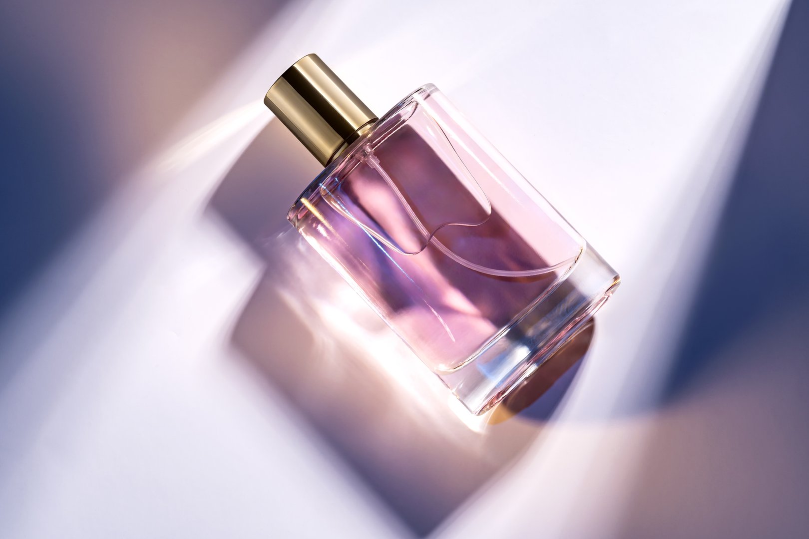 A glass perfume bottle with a golden cap on a white background with deep shadows and light effects. Trending showcase , product presentation.