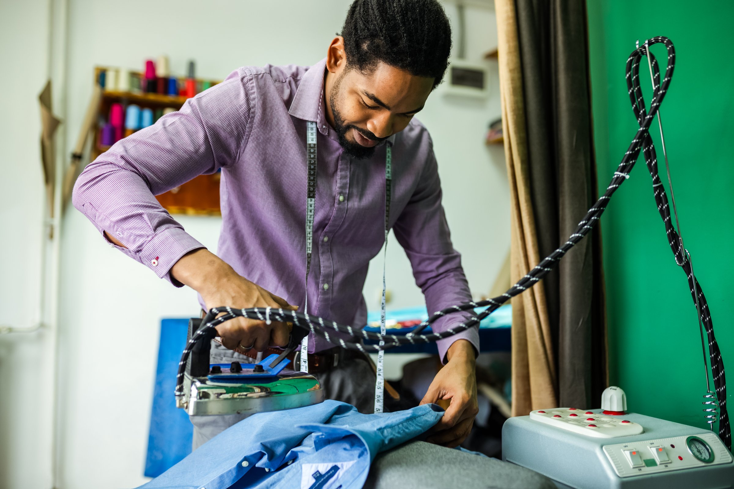 Young male African American tailor ironing shirt in his atelier.