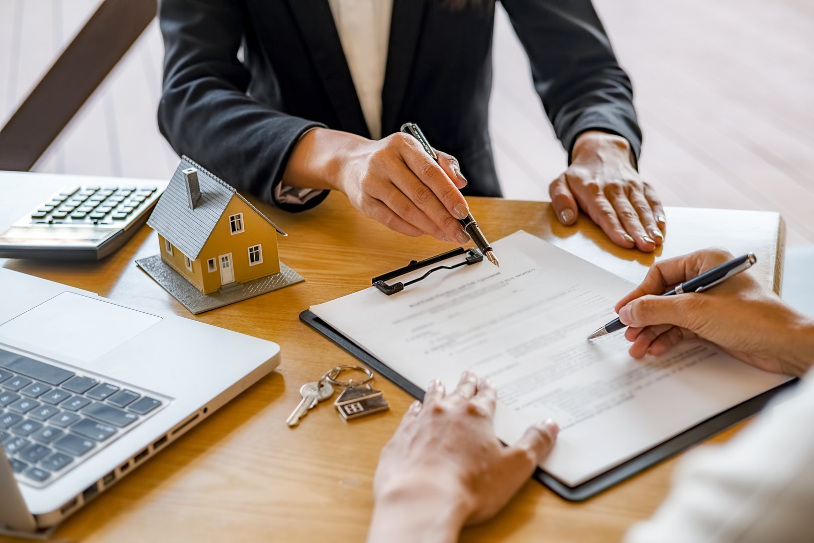 Cropped Hands Of Woman Signing Document With Female Real Estate Agent At Desk In Office