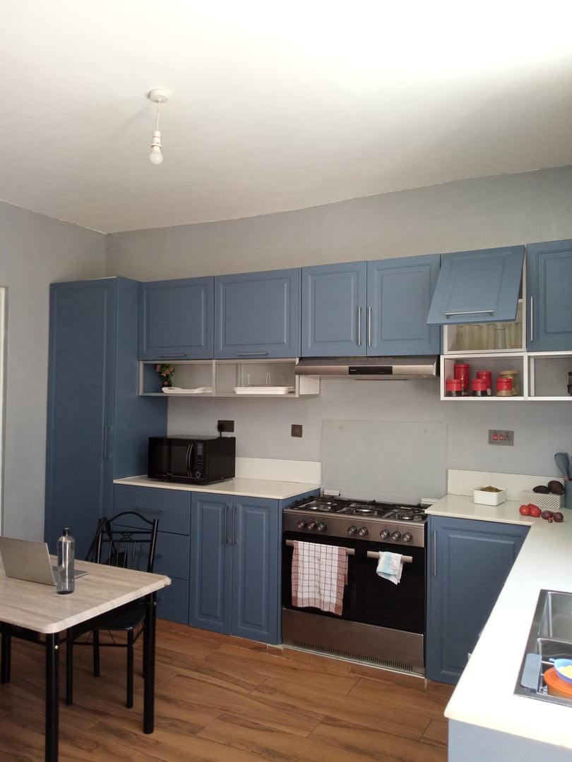 Modern kitchen with blue cabinets, gas stove, microwave, wooden floor, and small dining table with chairs.