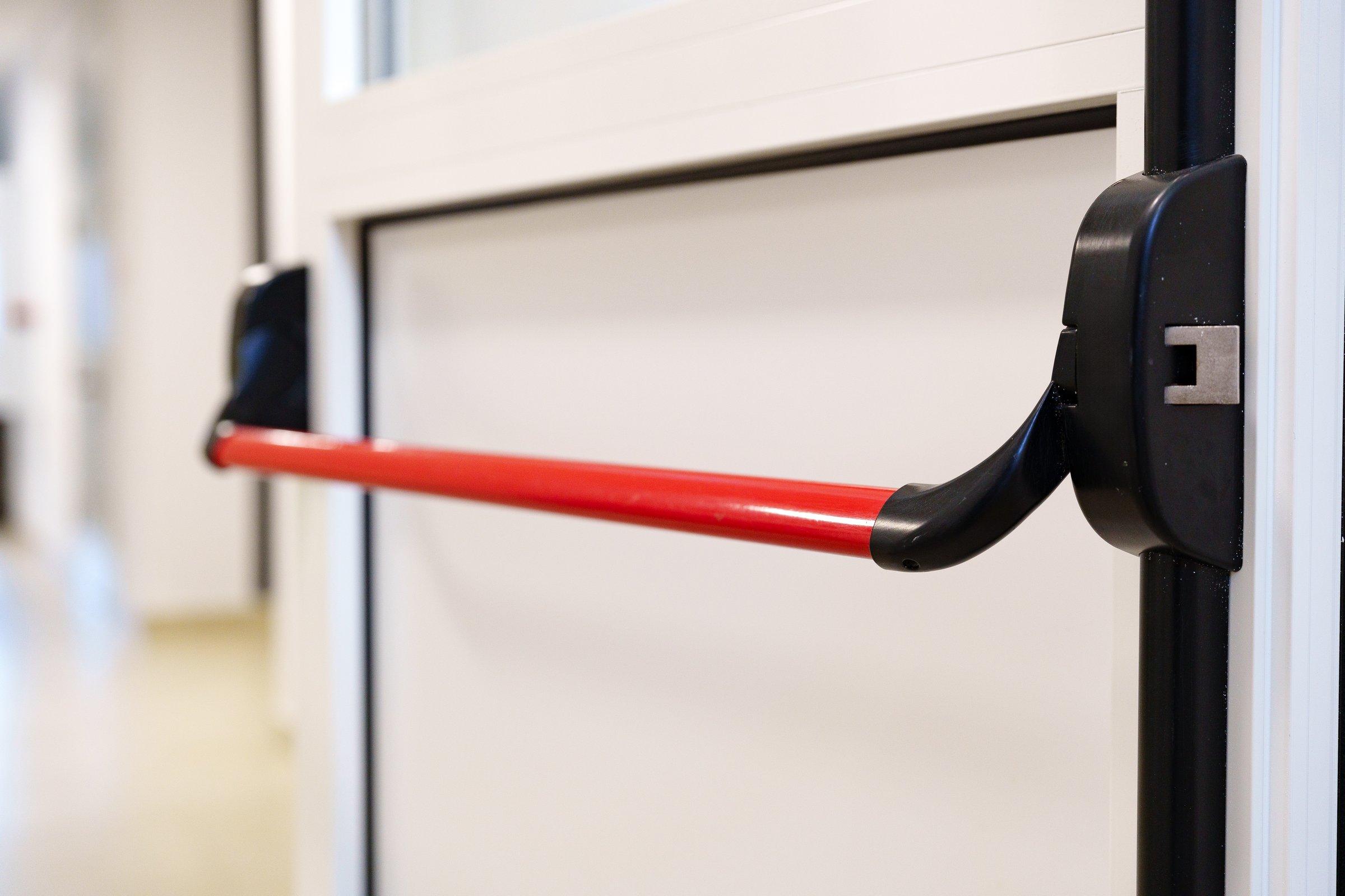 A red handle safety device is mounted on a door within a sleek commercial building corridor. This feature promotes accessibility and safe passage for all users.