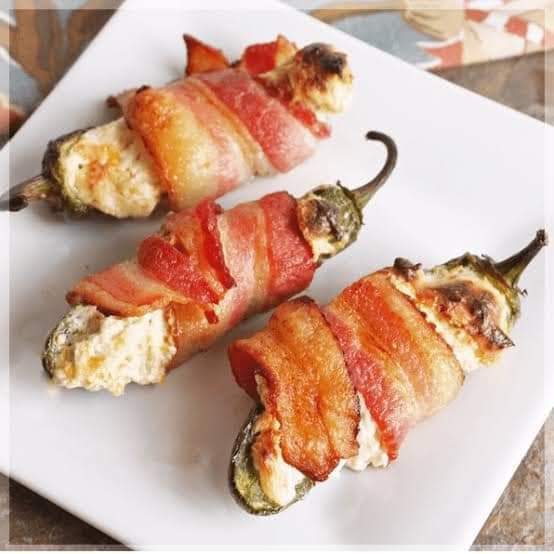 Three bacon-wrapped jalapeños stuffed with creamy cheese on a white plate.