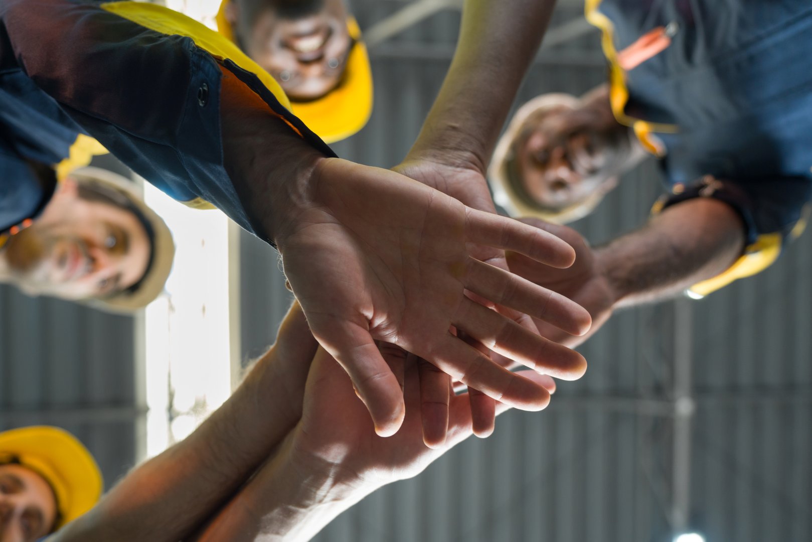 Group of male factory labor join hands together after finish meeting. Everyone wearing safety uniform and helmet. Worker are working in the factory. Bottom View