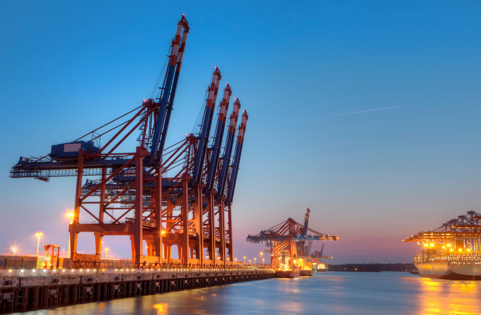 Harbor in Hamburg at night. In front you see the tower crane for the container ships. Background some container ships.