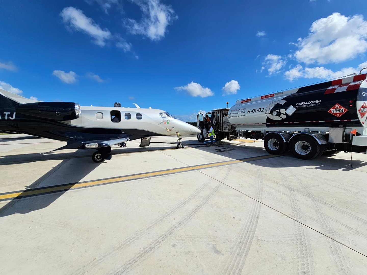 A small jet plane being refueled by a Capsacona fuel truck on an airport runway under a clear blue sky.