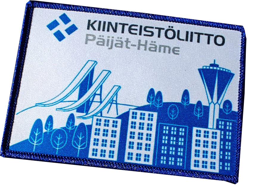 Embroidered patch featuring urban buildings, ski jumps, water tower, and text KIINTEISTÖLIITTO Päijät-Häme in blue.