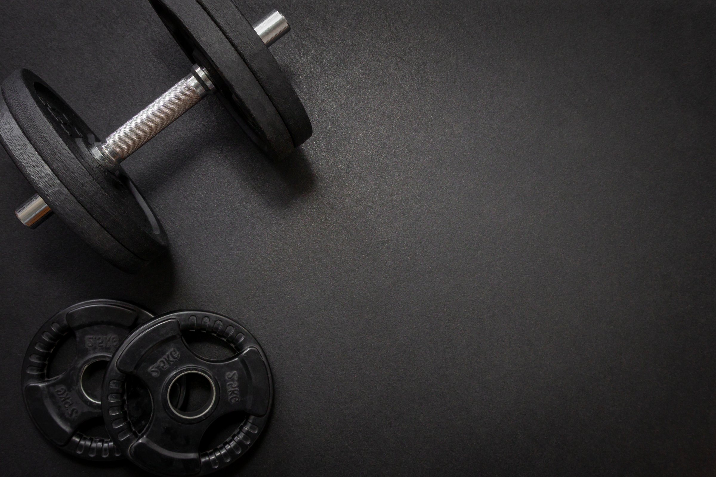 Black dumbbell and weights lying on a dark gym floor